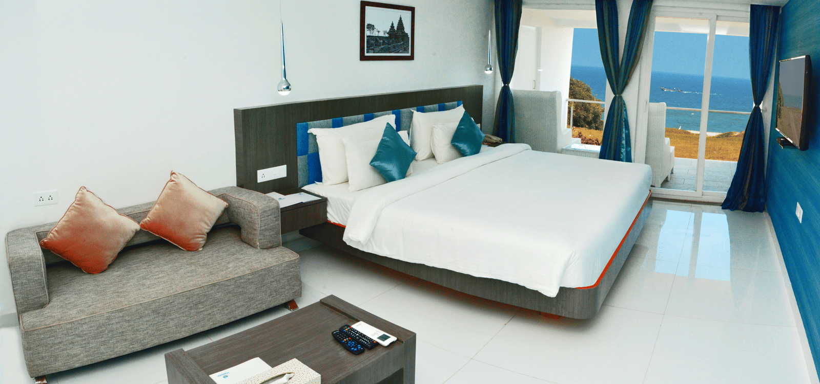 A clean, modern hotel bedroom with a large white bed, dark accent wall, and a small sitting area - Grande Bay Resort & Spa, Mamallapuram