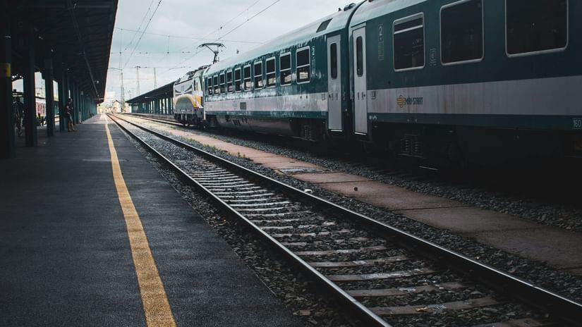 A railway platform with train on the track under a cloudy sky.