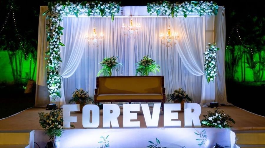 Chic wedding stage with sheer drapes, white florals, and a lit ‘FOREVER’ sign at Ilara Hotels & Spa, OMR, Chennai