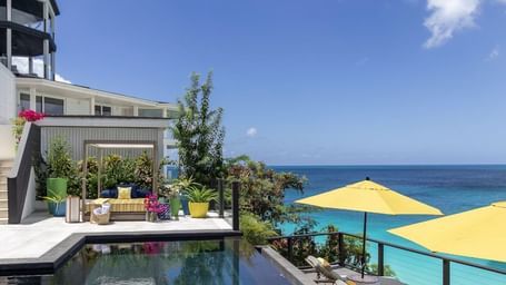 A poolside setting with ocean views at Tamarind Hills Resort and Villas Antigua, with two beach umbrellas and a canopy.
