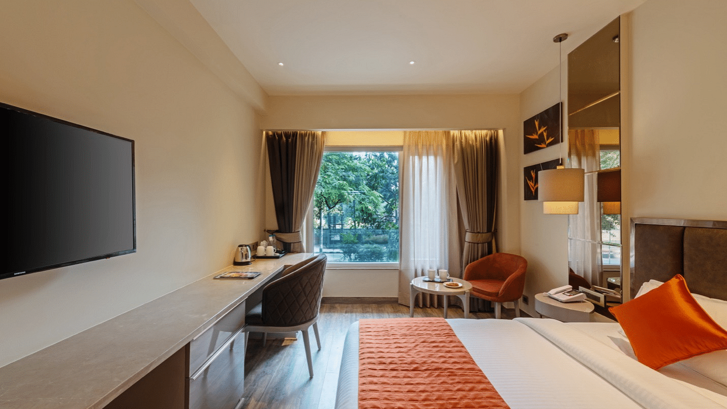 Hotel room with a made bed, desk, TV, window with natural light, orange runner, clean and tidy.