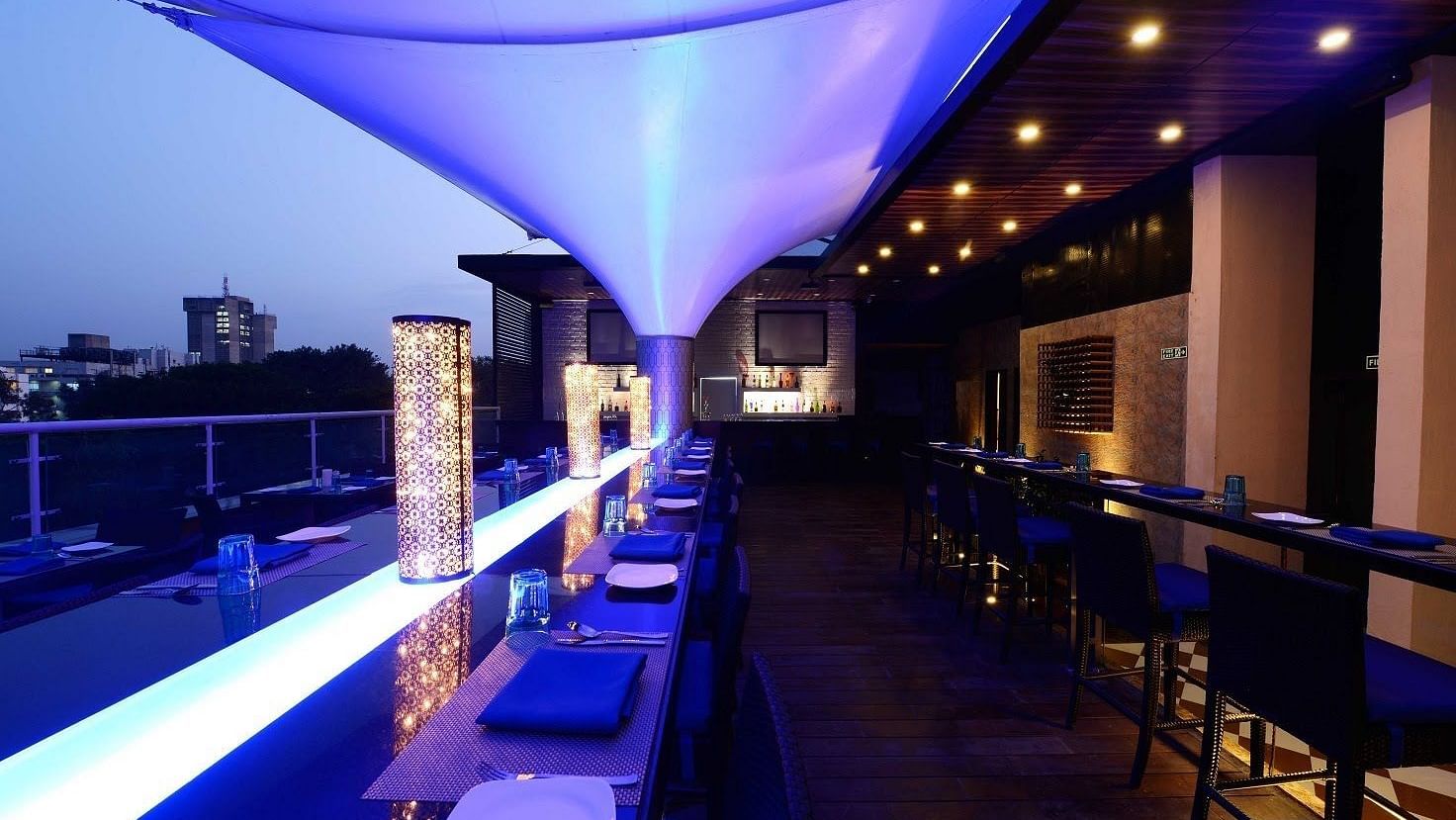 Skylit Rooftop Lounge and Bar at The Cunningham Hotel featuring ambient blue lighting, elegant seating, a modern bar, and a city skyline view at dusk