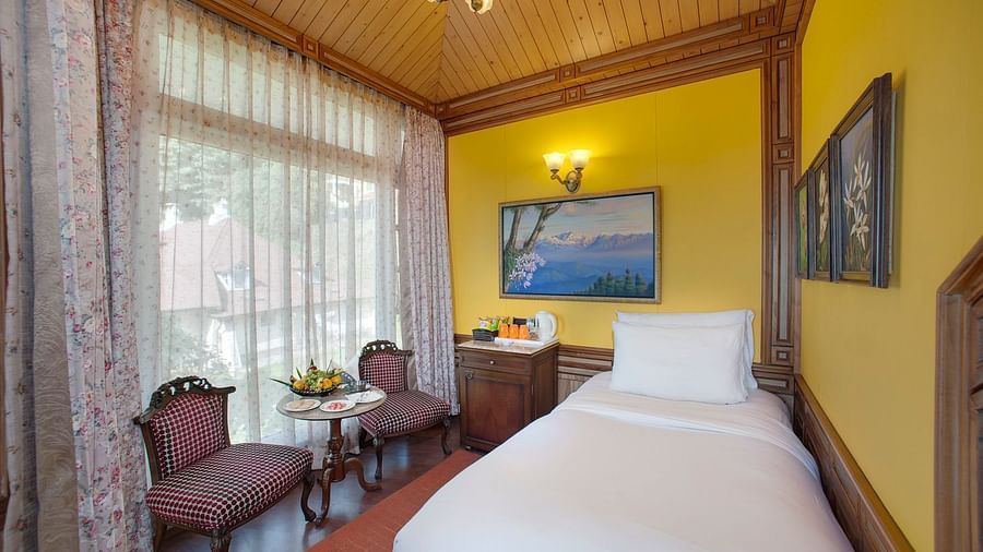 a king size bed perched in the corner of a room and a two chairs kept to its left - Mayfair Hill Resort, Darjeeling