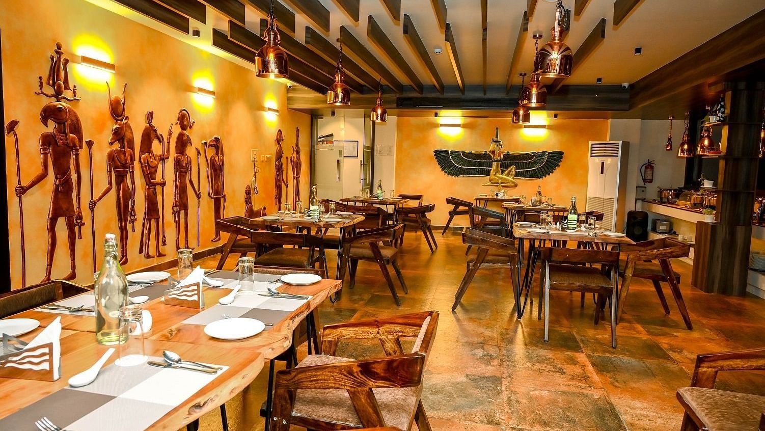 A side view of the restaurant dining area, showcasing set tables, the wooden ceiling, and the collection of decorative statues lining the walls - Sea Hills Hotels, Sri Vijaya Puram (Port Blair)