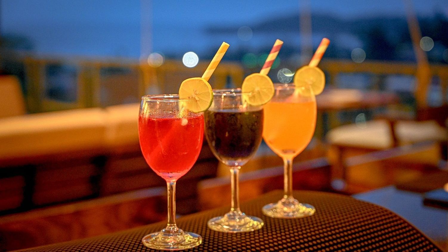 Three vibrant, colourful cocktails, two red and one orange, are arranged on a dark, reflective surface, likely a bar counter, with a blurred background - Sea Hills Hotels, Sri Vijaya Puram (Port Blair)