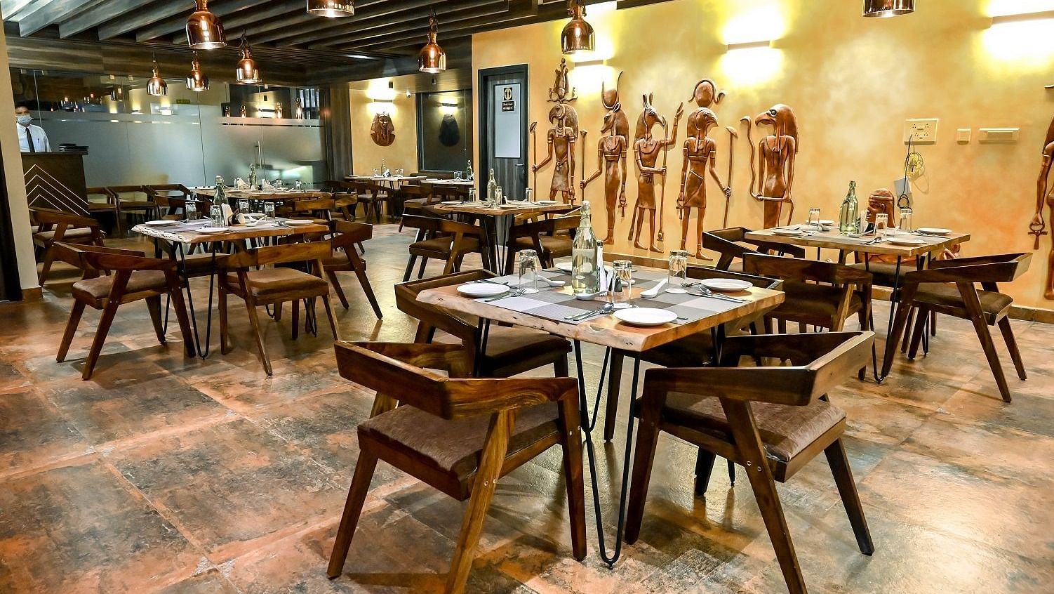 Another angle of the restaurant dining space, focusing on a few tables set with placemats and cutlery, against a backdrop of unique wall art - Sea Hills Hotels, Sri Vijaya Puram (Port Blair)