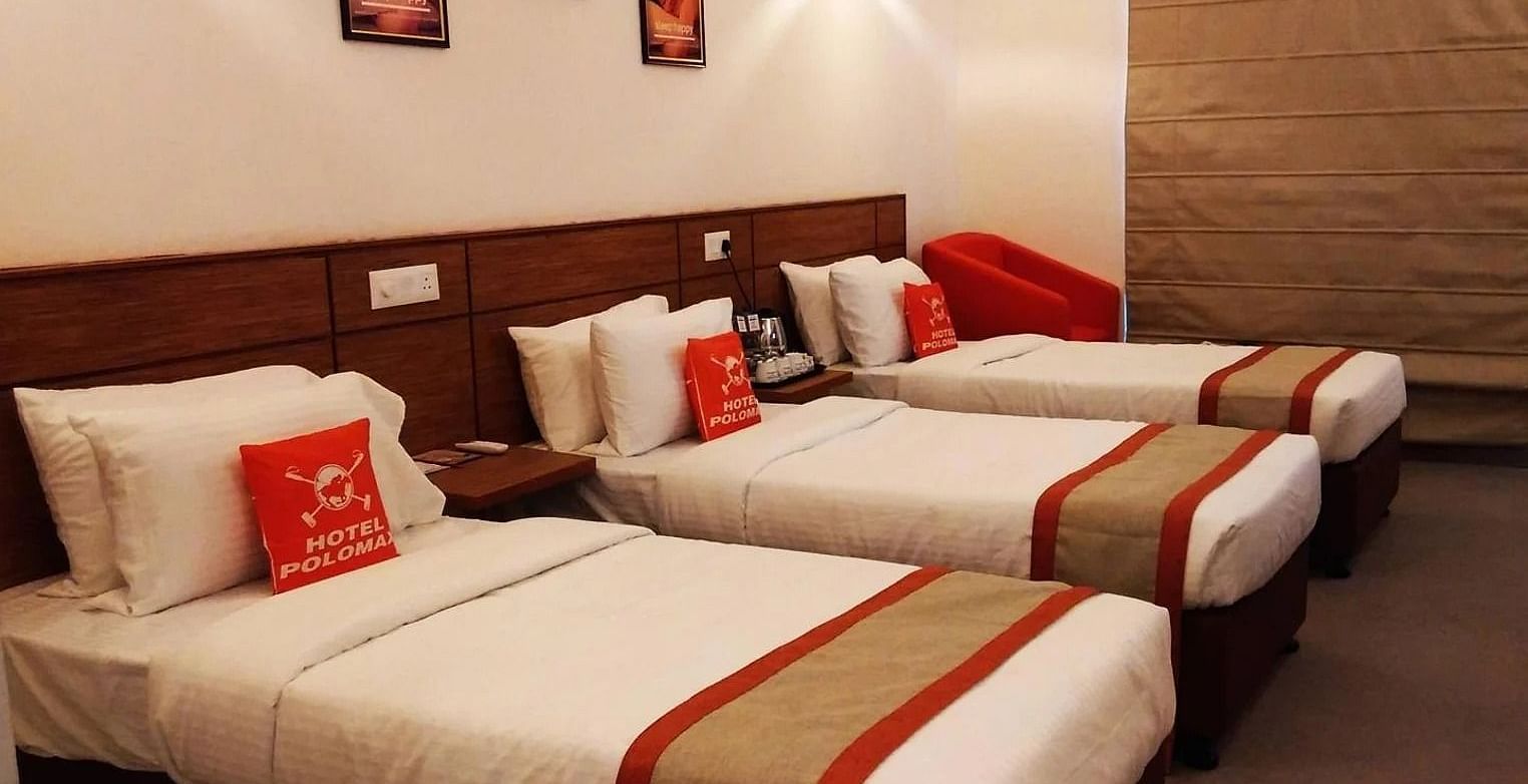 a room with three single beds with plush pillows along with a red cushion and tucked in comforters - Max Hotel Jabalpur