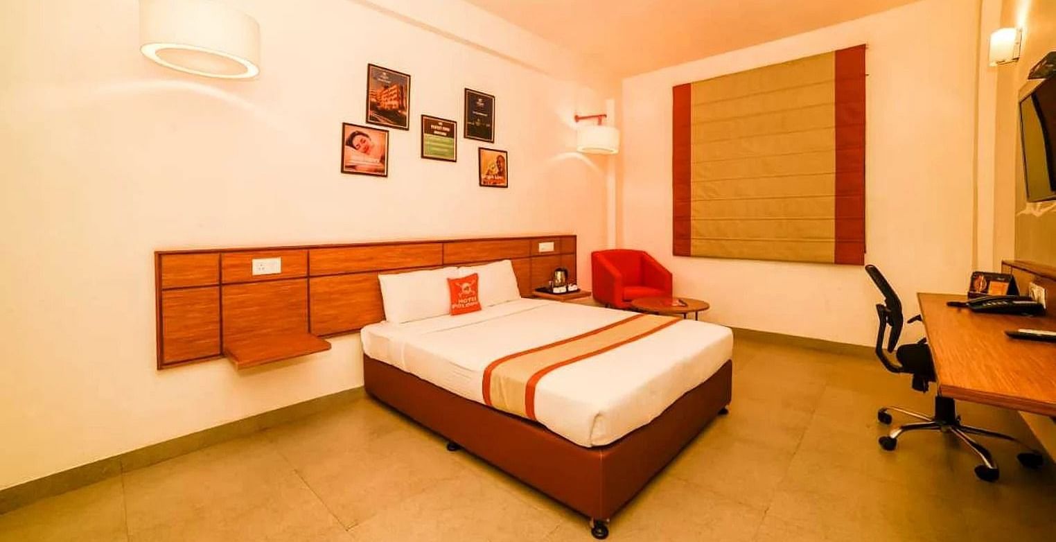 a spacious room with a queen size bed placed in the middle with small photo frames hung on the wall - Max Hotel Jabalpur
