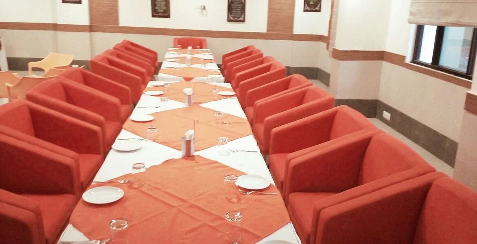 a long table featured in a spacious hall with big cushioned chairs around it - Max Hotel, Jabalpur