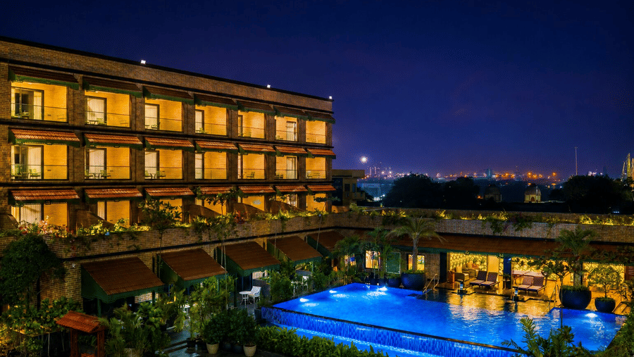 An illuminated outdoor pool lit up at night beside the multi-story brick building at MAYFAIR Bay Resort, Paradeep.