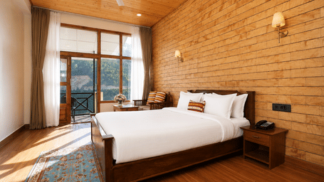 Junior Suite at Summit Rungkhung Village Resort - The Signature Collection containing a double bed, bedside table with phone, wall sconces, floor rug, seating area, and balcony doors.
