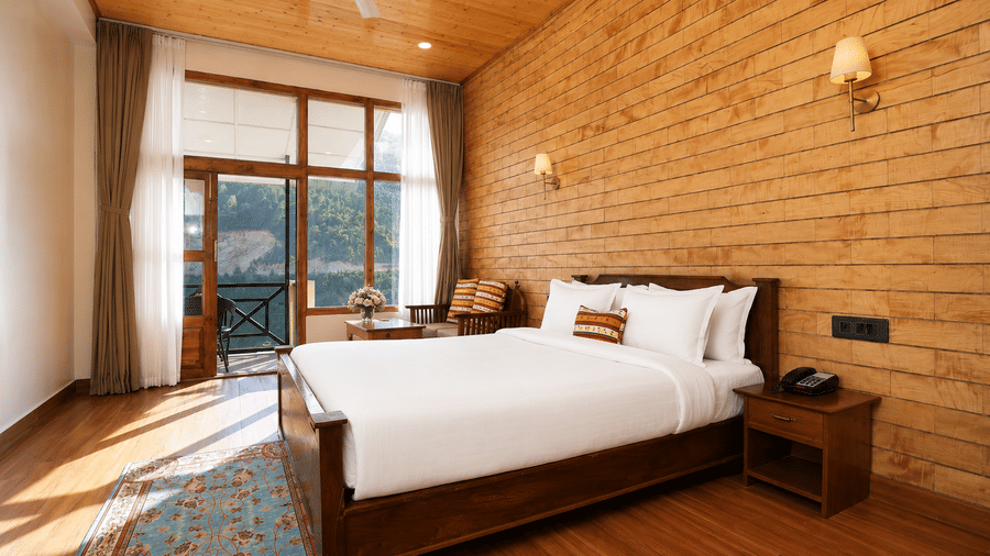 Junior Suite at Summit Rungkhung Village Resort - The Signature Collection containing a double bed, bedside table with phone, wall sconces, floor rug, seating area, and balcony doors.