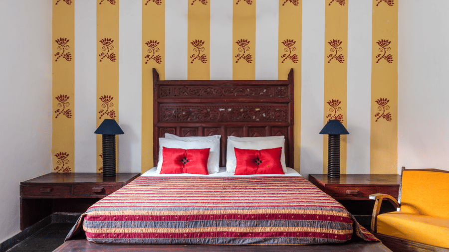 Double bed with red patterned bedding, a carved wooden headboard and matching bedside tables against striped walls.