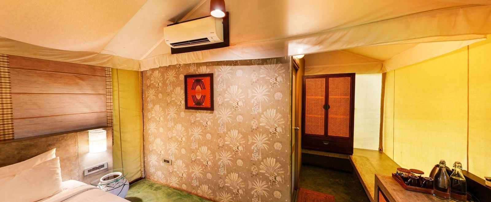 Interior of a tent room with yellow canvas walls, bed, A/c and luggage rack at Fireflies Resorts, Kabini.