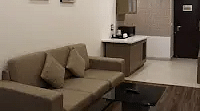 A cozy space with a plush couch and 2 artwork framed on the wall with a small table beside. - Golden Suites, Gurgaon