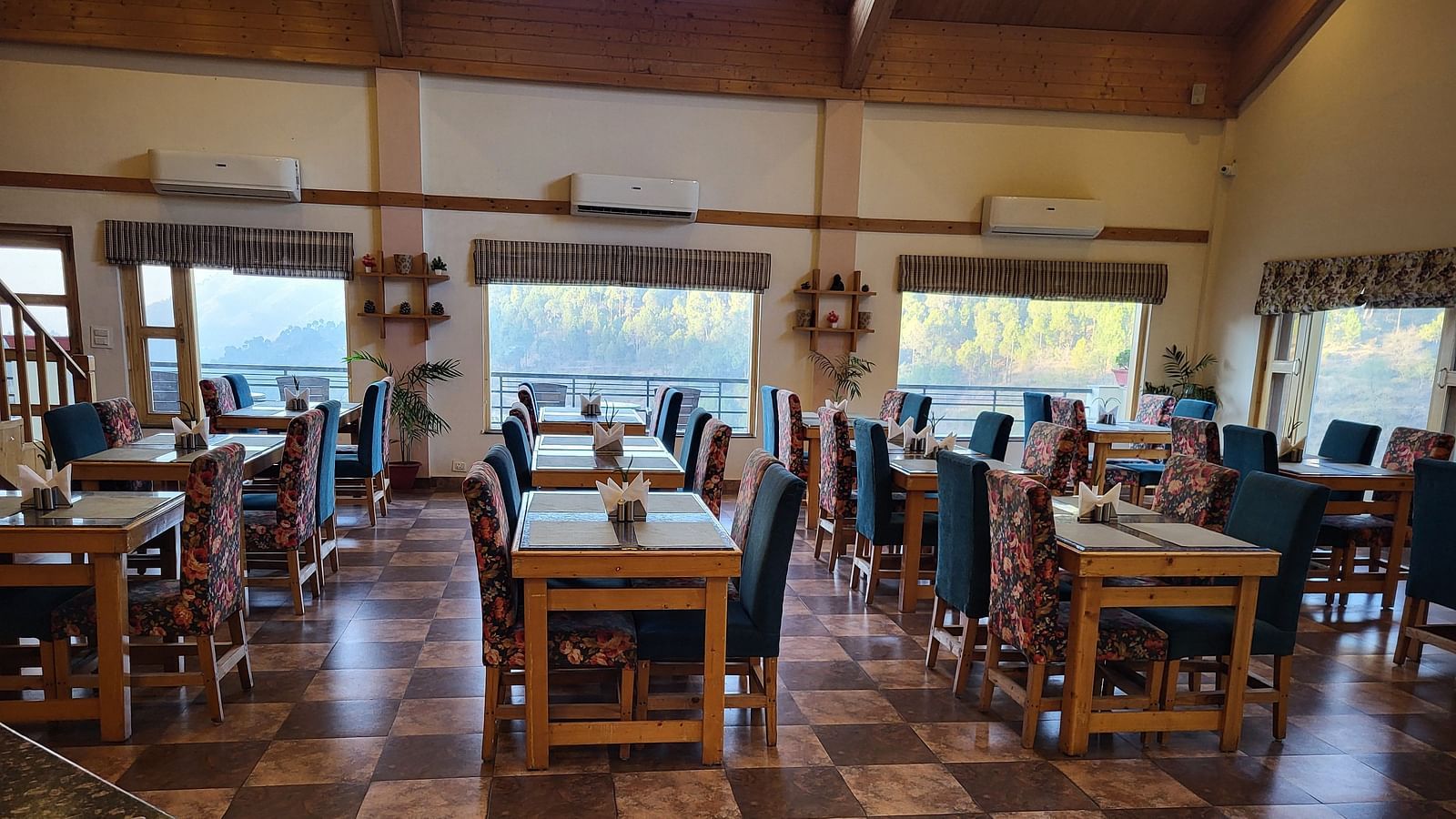 Spacious dining area with wooden furniture and large windows at Dagshai Manor Kasauli - Inde Hotels.