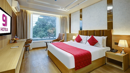 A bedroom at Hotel 91 HUDA Premier, Gurugram with a king size bed, runner, pillows, desk, chair wall-mounted TV, window, and an armchair.
