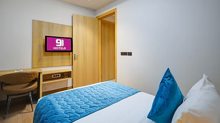 A bedroom at Hotel 91 HUDA Premier, Gurugram with a king size bed, chair, desk, wall-mounted TV, and wooden door.