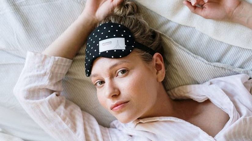 A woman lying in bed with an eye mask on her forehead, appearing relaxed and well-rested.