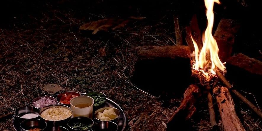 Jungle Cooking - Sajan - a thali meal of 10 items placed on the grass beside a camp fire.