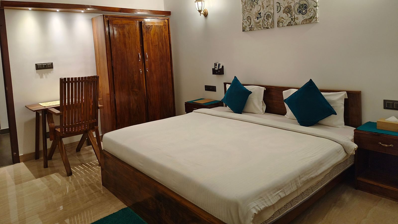 Wide view of a double bed with blue pillows, a chair and a cupboard in 102 room at Ananda Holiday Home, Wayanad 9