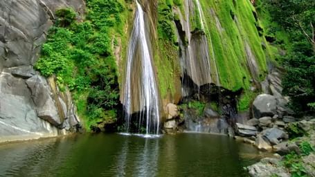 Bheel Beri Waterfalls in Rajasthan featuring water cascading down the rocky mountain surrounded by plants. At the bottom there is a pond where water gets collected.