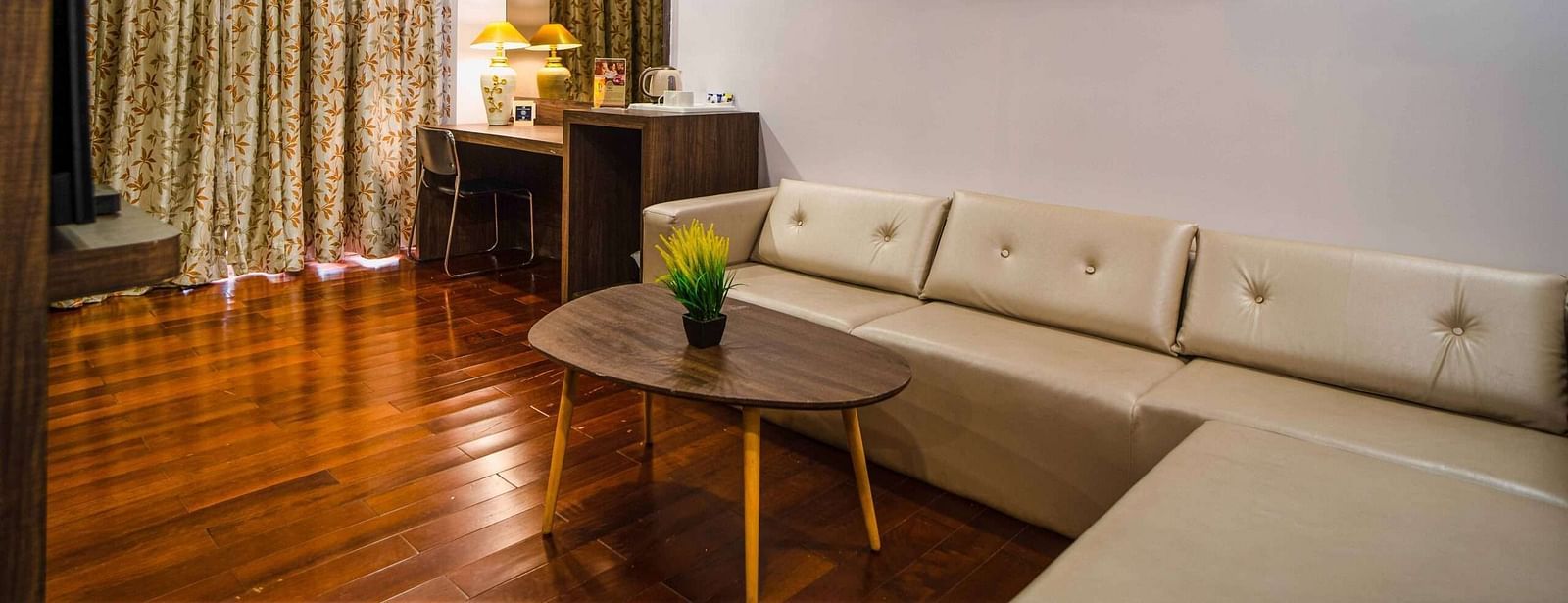 A spacious room Mansha Hotel Regency offering a sofa, a coffee table, a work desk, a chair, and an artwork hung on the wall.