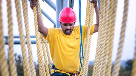 A smiling man in a red helmet navigates a challenging thick rope course - District Gravity Adventure Park, Hyderabad