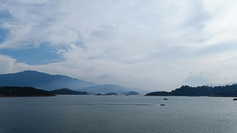 A tranquil lake stretches under a vast sky with rolling hills in the distance.
