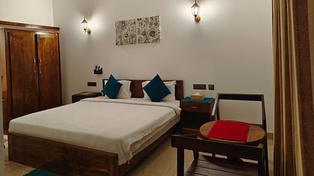 Another angle of a double bed with blue pillows, two chairs facing each other and a frame on the wall in102 room at Ananda Holiday Home, Wayanad 5