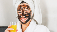 a woman with a face mask in bathrobe holding a glass of juice 