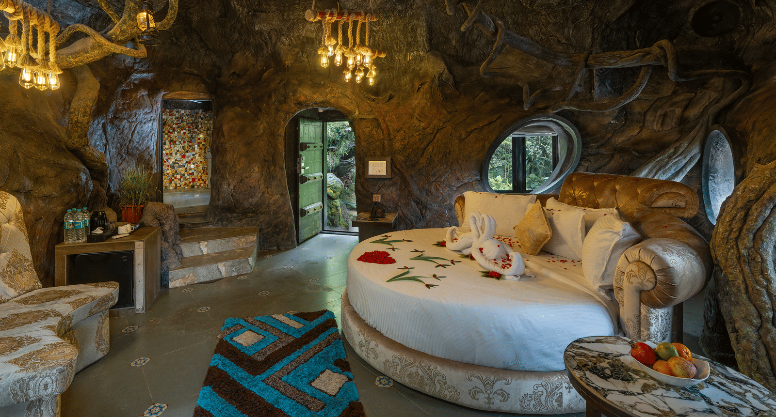 The bedroom of the Cave Room at Parakkat Nature Hotel and Resorts, Munnar, featuring a large circular bed, decorative light fixtures, and walls designed to resemble natural rock formations.