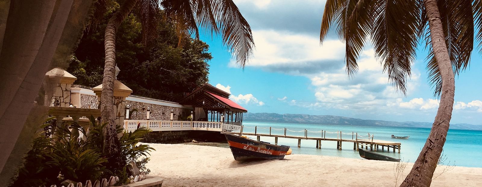 a beach with a boat, coconut trees and a shack on it with the sea in the background