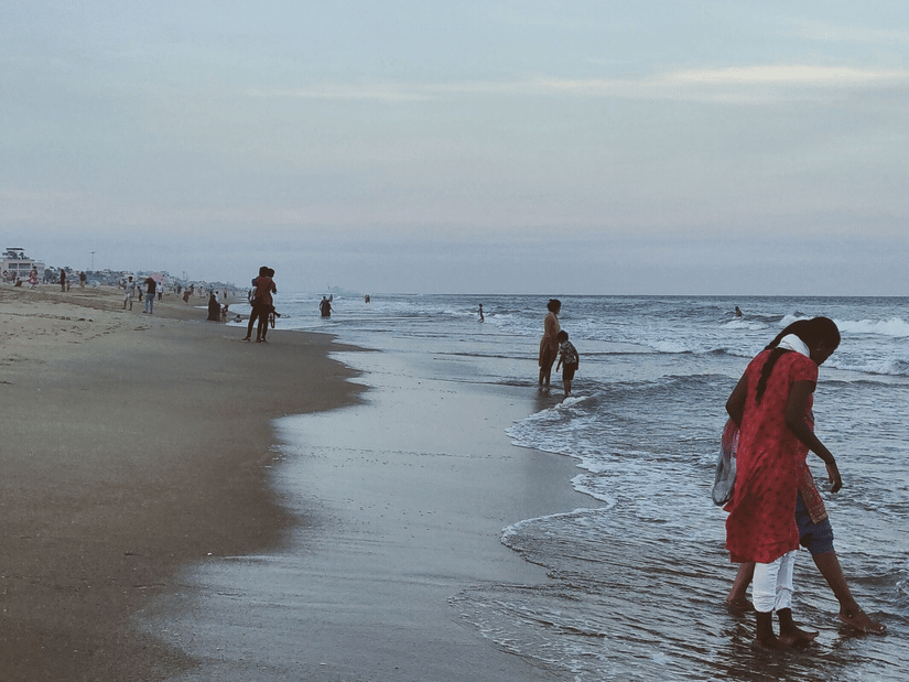 A beach with a woman standing in shallow water. There are more people in the background.