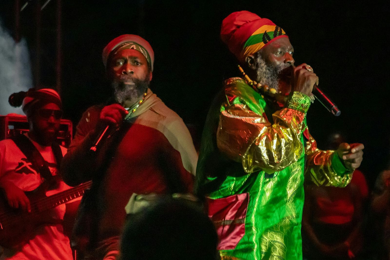 Two Reggae artists singing on stage during the night wearing colourful clothes.