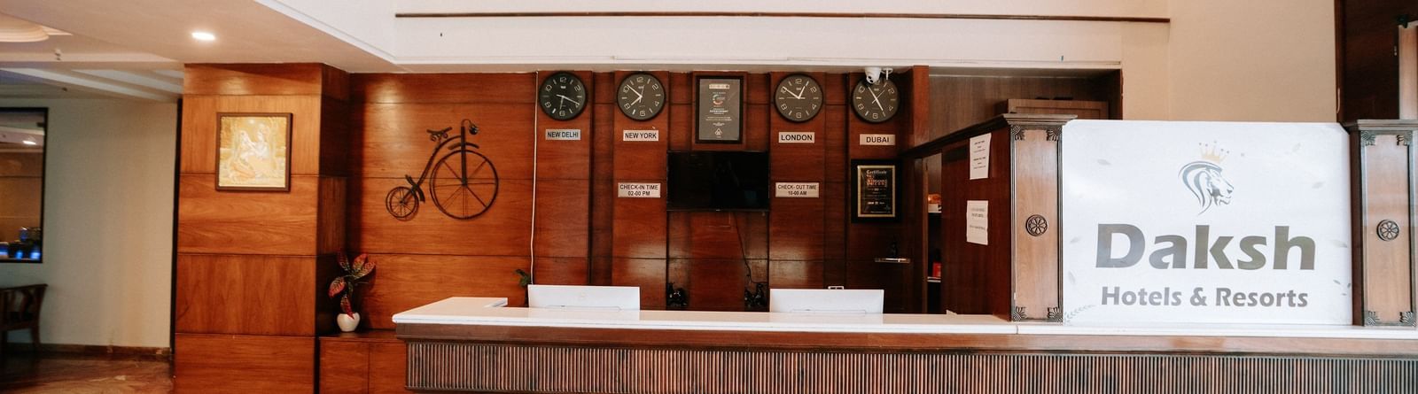 The hotel reception desk with a dark wood finish and a marble-effect floor at Daksh The Madhuvan Suites, Dwarka.
