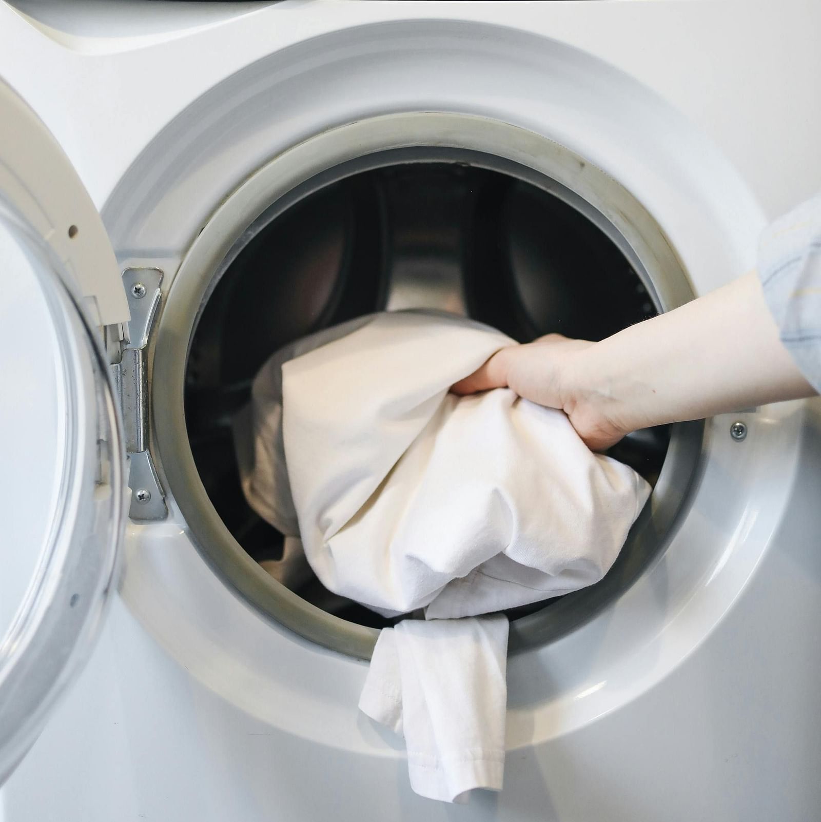 A hand putting clothes in a washing machine.