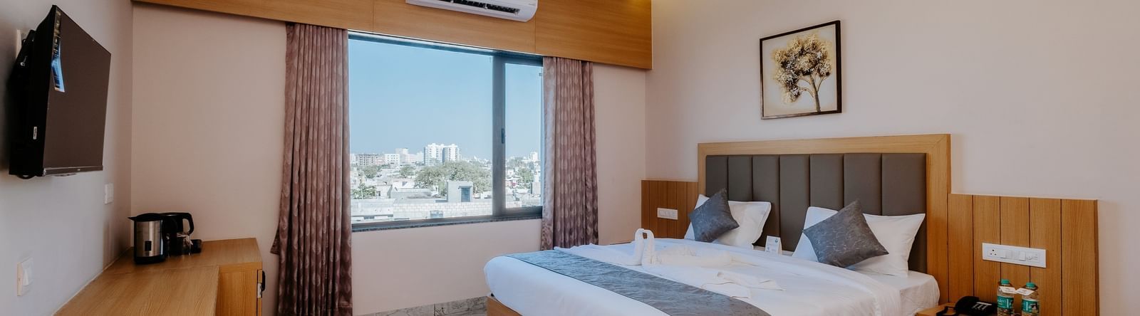 A well-appointed bedroom at Daksh The Grand Gowardhan, Dwarka, featuring a comfortable double bed, television, and window featuring views of the city.