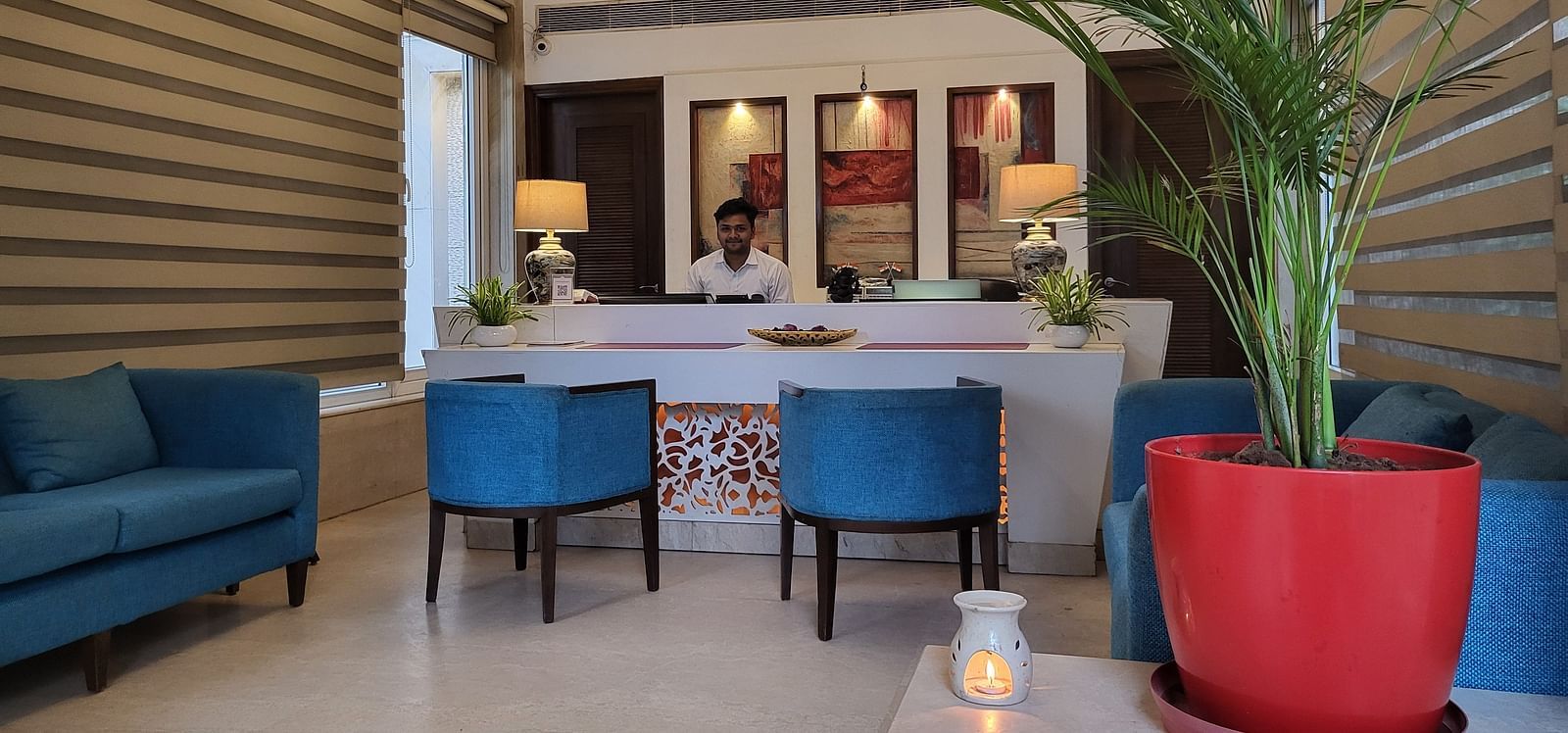 A reception lobby featuring sofas, chairs, reception desk where a receptionist is sitting, and lights hanging from the ceiling - Inde Hotel Signature Tower Gurgaon
