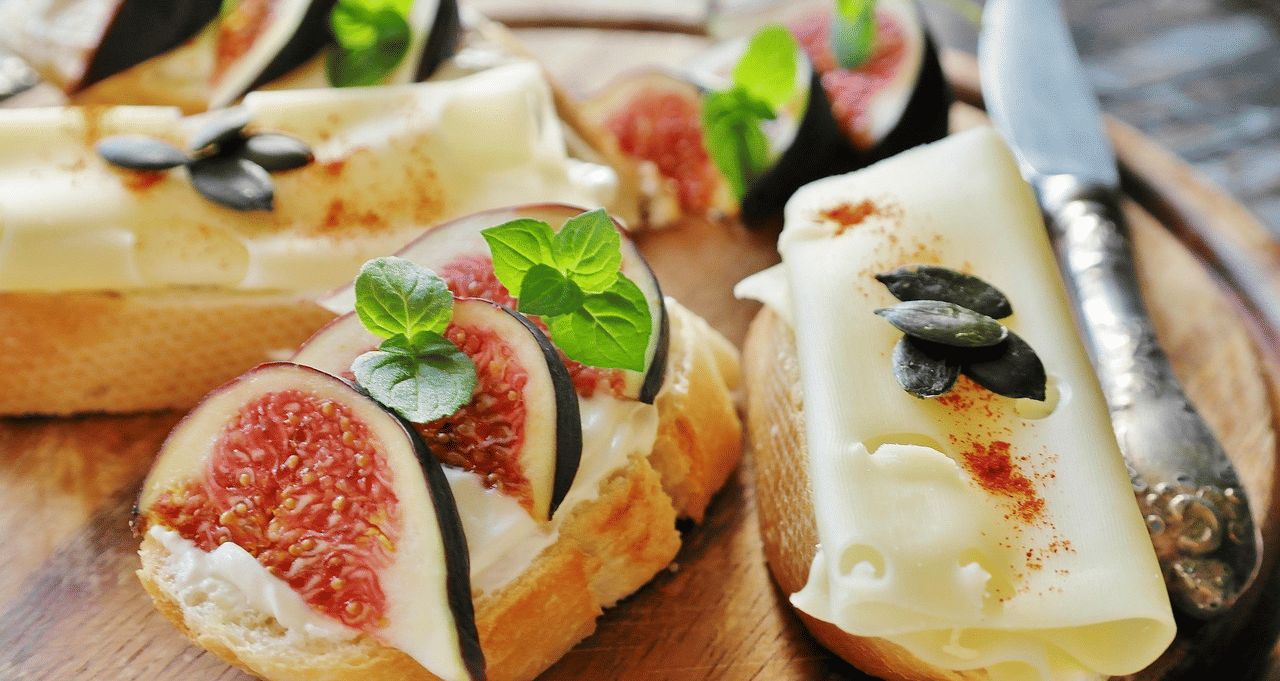 A serving board with pieces of bread topped with fig, herbs, and cheese slices.