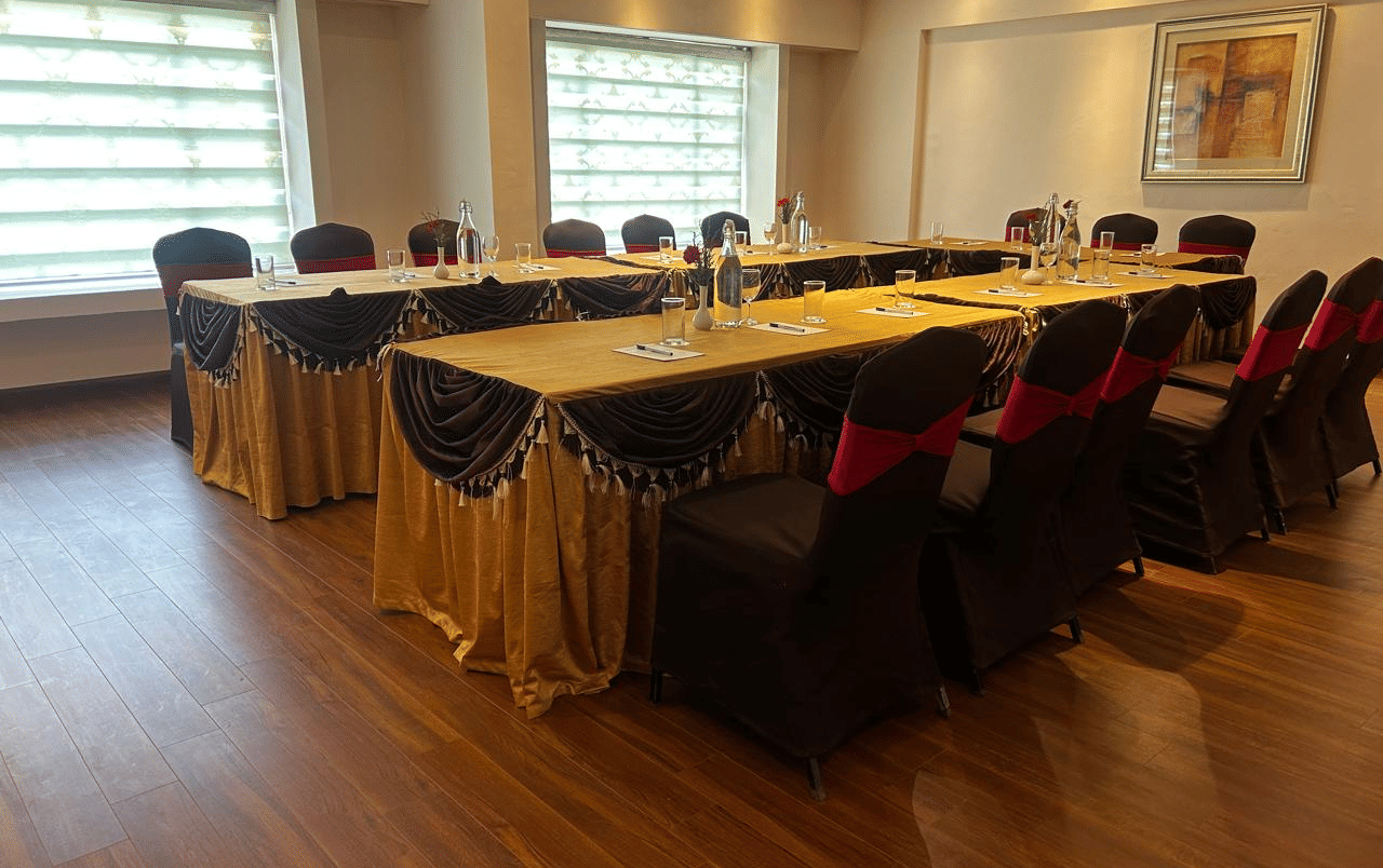 A banquet hall at Accord Highland Ooty, featuring a U-shaped table setup and chairs with red sashes.
