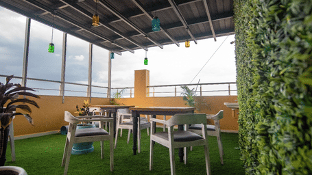 A bright rooftop dining terrace with artificial grass, white modern chairs, and a decorative green wall at The Bull Boutique Hotel.