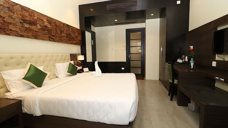 A clean and spacious hotel bedroom with a large bed, featuring modern wooden and textured wall finishes and an open doorway leading to another part of the room - Sea Hills Hotels, Sri Vijaya Puram (Port Blair)