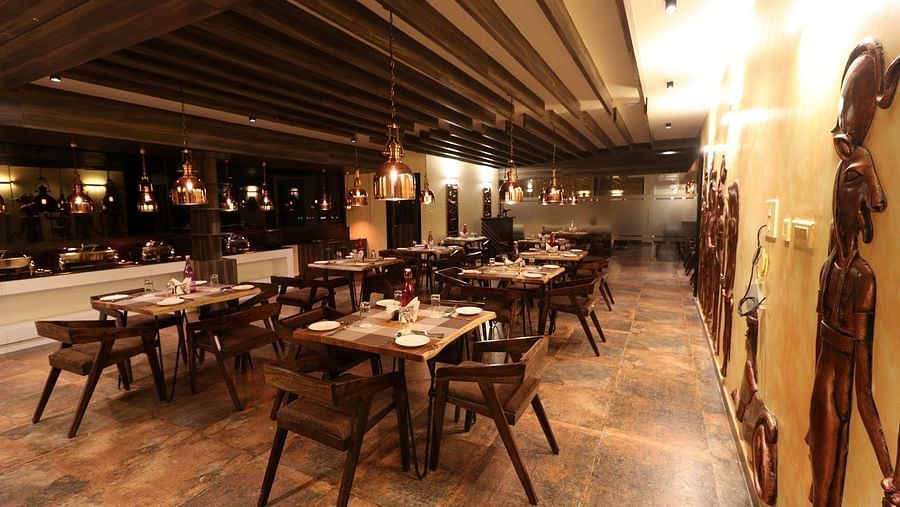 Another wide shot of the restaurant, highlighting the arrangement of dining tables, the warm lighting, and the unique, elongated statues adorning the walls - Sea Hills Hotels, Sri Vijaya Puram (Port Blair)