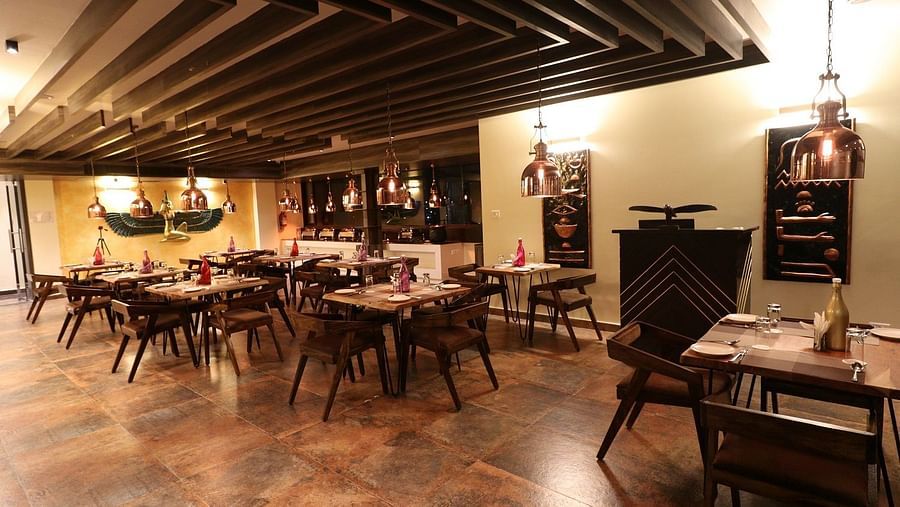 A warm and inviting restaurant or dining area with numerous wooden tables and chairs, a dark patterned ceiling, and soft lighting - Sea Hills Hotels, Sri Vijaya Puram (Port Blair)