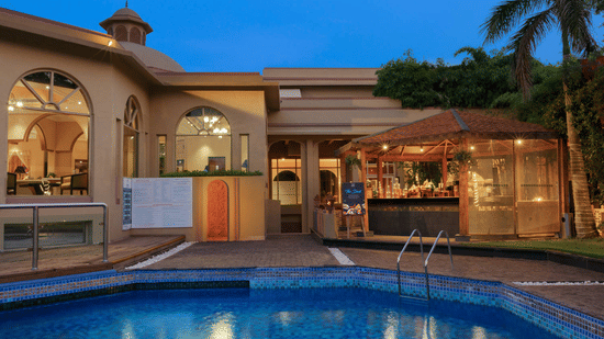 Facade of Heritage Village Resorts and Spa, Manesar with Rajasthani architecture and a pool in the foreground.