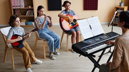  A group of children engaging in a music session, playing various instruments including a keyboard, guitar, ukulele, and flute, in a room with a cozy, creative atmosphere.