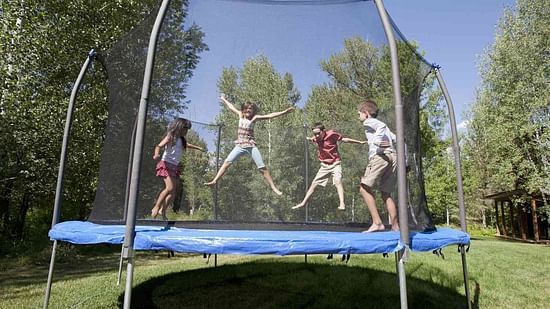 Children gleefully jump on an outdoor trampoline, enclosed by a safety net, enjoying playful moments in a lush green backyard.