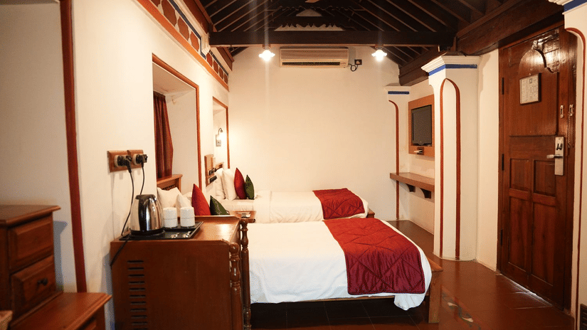 A cozy bedroom at Chidambara Vilas - A Luxury Heritage Resort, with twin beds, wooden walls and ceiling, and simple furnishings.