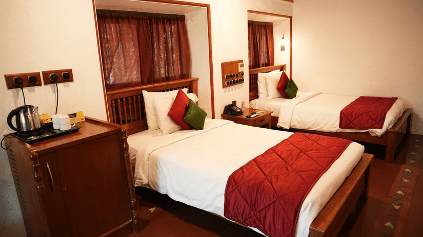 A room at Chidambara Vilas - A Luxury Heritage Resort, featuring twin beds in the background, both with linens, and wooden furniture.